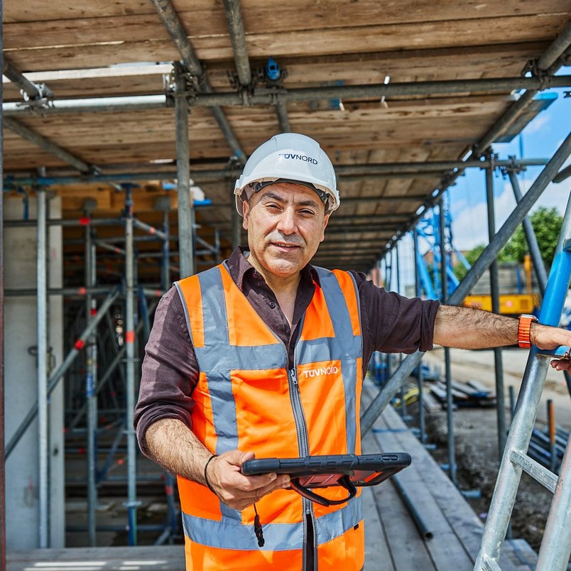 Contact opnemen met TÜV NORD Medewerker van TÜV NORD staat in een bouwomgeving klaar om contactvragen te beantwoorden.