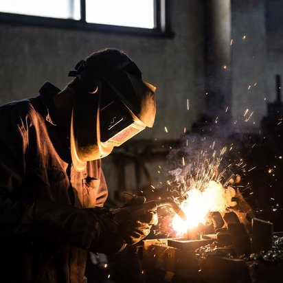 Vraag een offerte aan bij TÜV NORD voor Lastechniek Lasser met beschermhelm voert laswerk uit in werkplaats met vonken en fel licht.