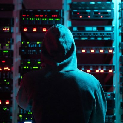 Vraag een offerte aan bij TÜV NORD voor ISAE 3000 rapport (SOC 2) Persoon met capuchon in een datacentrum als illustratie van cyberdreiging of hacking.