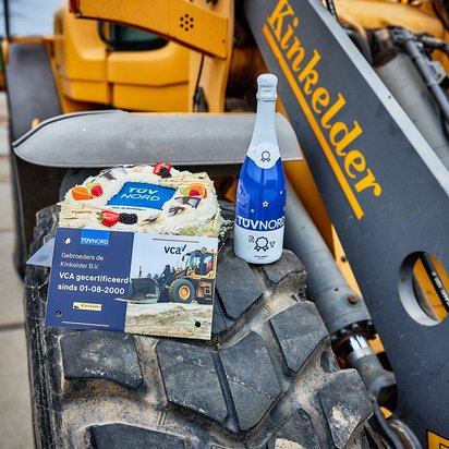 Vraag een offerte aan bij TÜV NORD voor VCA certificering Viering van VCA-certificering met taart en fles op bouwmachine.